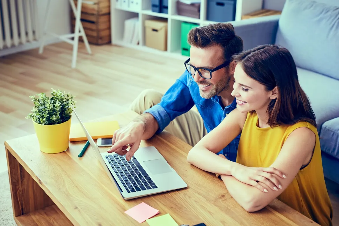 Smiling couple reviewing a laptop together at a coffee table
